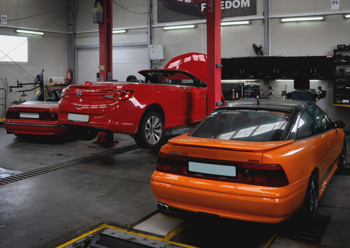 Opel Cascada roșu și Opel Calibra portocaliu pe lift - reparații motoare Service Adam Cluj
